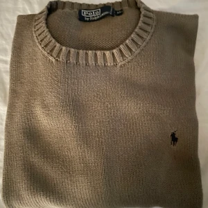 Beige stickad tröja Polo Ralph Lauren - Snygg beige stickad tröja från Polo Ralph Lauren med klassisk rund halsringning och broderad logga på bröstet. Perfekt för dig som gillar en stilren och tidlös look. Passar lika bra till jeans som till chinos.