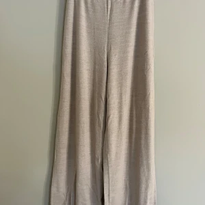 Beiga wide byxor från NA-KD - Snygga beiga byxor från NA-KD i storlek M. De har en loose och wide passform med hög midja och är tillverkade i ett mjukt, stickat material. Perfekta för en chill och avslappnad look.