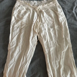 Beiga linnebyxor från Roxy med snörning - Luftiga beiga linnebyxor från Roxy med elastisk midja och grov snörning framtill. Byxorna har två stora fickor fram och avslappnad passform, perfekta för varma dagar och chill vibes.