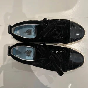 Svarta sneakers från Lanvin - Snygga svarta sneakers från Lanvin i en kombination av mocka och lackdetaljer. Skorna har en klassisk snörning och en vit sula som ger en stilren kontrast. Perfekta för en trendig look.