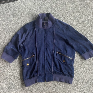 Mörkblå tunn cardigan från Vero Moda - Snygg mörkblå tunn cardigan från Vero Moda med trekvarts ärmar och ribbade muddar. Jackan har dragkedja framtill, två fickor med dragkedja och knappdetaljer. Materialet är lätt strukturerat och ger en cool känsla. Perfekt för dig som vill ha en unik jacka med streetvibe. Vintage❤️