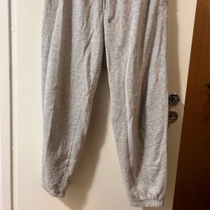 Grå mjukisbyxor med snörning - Säljer ett par grå mjukisbyxor med elastisk midja och snörning. Byxorna har avslappnad passform, resår vid benslut och är tillverkade i mjukt bomullsmaterial. Perfekta för chill dagar eller när du vill vara extra bekväm.