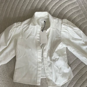 Vit jacka med puffärm från Zara - Helt ny snygg vit jacka från Zara med puffade axlar och klassisk krage. Skjortan har knappar framtill och är tillverkad i ett mjukt bomullstyg. . Storlek M.