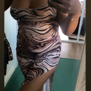 Zebramönstrad långklänning med slits - Snygg långklänning med zebramönster i beige, brun och svart. Klänningen är axelbandslös och har en hög slits på sidan som ger en cool vibe. Materialet är stretchigt.