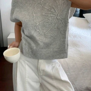 Grå stickad topp med blommönster - Superfin grå stickad topp med korta ärmar och ett stort, diskret blommönster framtill. 