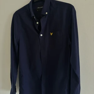 Mörkblå skjorta från Lyle & Scott - Snygg mörkblå skjorta från Lyle & Scott med klassisk krage och vita knappar. Knappt använd, kommer i mycket bra skick. 
