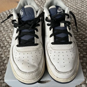 Nike Air Force 1 Low vit/marinblå - Nike Air Force 1 Low sneakers i vitt och marinblått skinn med silverfärgad swoosh. Klassisk perforerad tå, svart snörning och mörkblå yttersula. Ikonisk streetstil med lågt skaft och bekväm passform. Perfekta för dig som gillar retrovibbar och tidlös design. Ord. Pris: 1400kr, säljes för 300kr inkl originalkartong