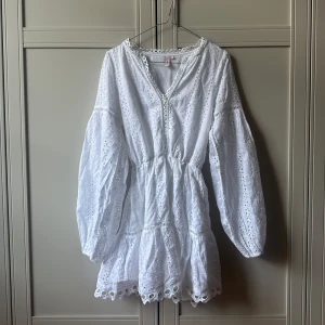 Vit broderad klänning från Nelly - Superfin vit klänning från Nelly med broderade detaljer och hålmönster. Klänningen har långärmade puffärmar, v-ringad hals och volang i midjan. 💕