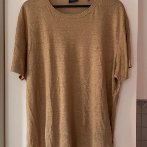 Beige t-shirt från GANT - Snygg beige t-shirt från GANT med diskret logga på bröstet. Modellen är klassisk med rund hals och korta ärmar. Materialet känns mjukt och lätt, perfekt för chill dagar. Passformen är översize och färgen är neutral vilket gör den enkel att matcha.