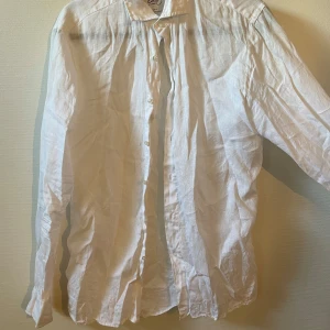 Vit linneskjorta från Oscar of Sweden - Snygg vit skjorta i linne från Oscar of Sweden, slim fit-modell med klassisk krage och knappar framtill. Långärmad och luftig, perfekt för varma dagar. Stilren och enkel design som passar till många olika looks.