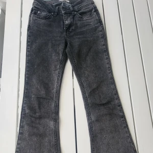 Svarta bootcut jeans med tvättad look - Snygga svarta jeans med tvättad finish och bootcut-ben. Klassisk femficksmodell med dragkedja och knapp framtill. Jeansen har en högre midja och är tillverkade i mjukt denimtyg som sitter skönt på kroppen.