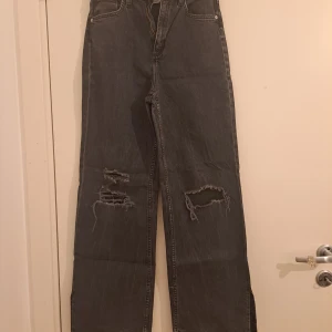 Svarta wide jeans från H&M, high waist - Säljer ett par svarta wide fit jeans från H&M med hög midja och justerbar midja. Jeansen har slitna detaljer och hål på båda benen för en cool, avslappnad look. Perfekta för dig som gillar streetstyle och vill ha bekväma jeans med attityd.