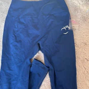 Mörkblå leggings från Peach - Snygga mörkblå leggings från Peach med hög midja och stretchigt material. Perfekta för träning eller chill, med diskret logga på höften. Sitter tight och formar sig efter kroppen för en clean look.
