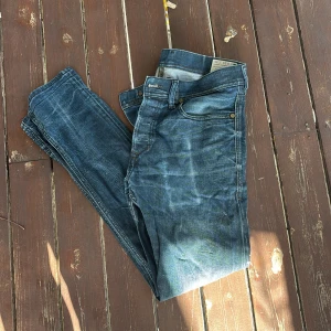 Diesel Tepphar slim jeans blå - Säljer ett par blå Diesel Tepphar jeans med slim-carrot passform. Jeansen har klassiska fem fickor, snygga slitningar och stretchigt material för extra komfort. Snygga kontrastsömmar och Diesel-logga på bakfickan. Perfekta för dig som gillar en modern och smal siluett.