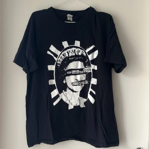 Svart t-shirt med tryck från Fruit of the Loom - Svart t-shirt från Fruit of the Loom i storlek L. T-shirten har ett stort vitt grafiskt tryck på framsidan med coolt motiv. Klassisk passform med rund hals och korta ärmar. Tillverkad i mjuk bomull som är skön att ha på sig.