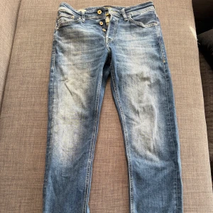 Blå tapered jeans från Jack & Jones - Snygga blå jeans från Jack & Jones i modellen Tapered/Mike. Jeansen har en klassisk femficksdesign, knäppning med knappar och coola slitningar framtill. Tillverkade i mjukt denimtyg med gul kontrastsöm på insidan. 🙌