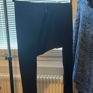Svarta tighta byxor från Vila - Svarta byxor från Vila i tight passform med dragkedjor vid bensluten. Byxorna har en enkel design och är gjorda i ett stretchigt material som sitter snyggt på kroppen. Storlek medium men väldigt töjbara.