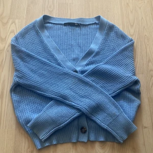 Blå stickad kofta - Superfin ljusblå stickad kofta från 157 med v-ringning och tre knappar framtill. Modellen är croppad med breda ribbade muddar vid ärmslut och nederkant. Perfekt att slänga över en topp för en chill look.