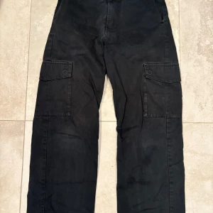 Svarta cargo byxor från Sweet SKBTS - Svarta cargopants med raka ben och stora fickor på sidorna. Byxorna har en avslappnad passform och passar S/M.