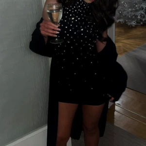Svart kort klänning, öppen rygg och  med pärlor - Supersnygg svart kort klänning med höghalsad design och pärldetaljer över hela framsidan. Ärmlös modell som ger en chic och festlig look, perfekt för att sticka ut på festen. (Använd en gång)