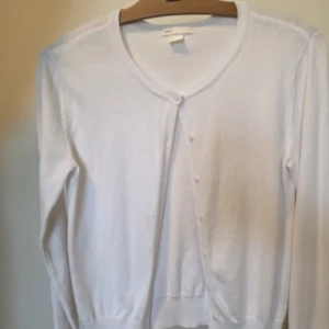 Vit kofta från H&M BASIC, storlek S - Klassisk vit kofta från H&M BASIC i storlek S. Materialet är mjukt och tunt, perfekt för lager-på-lager. Har liten gul stain på handen men det syns inte mycket. Kan träffas i odenplan, annars står inte för frakt  