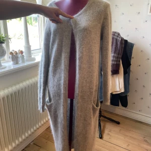 Ljusgrå lång kofta från Vila - Säljer en supermjuk och fluffig ljusgrå lång kofta från Vila. Koftan har öppet framtill, två stora fickor och är tillverkad i en mix av angora och nylon. Den är lite nopprig på insidan, men inget som syns när man har den på sig.