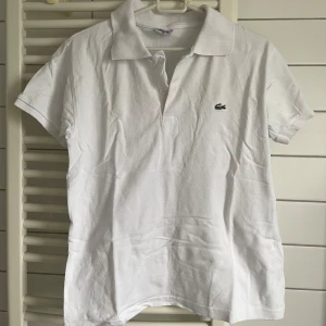 Vit pikétröja från Lacoste - Klassisk vit pikétröja från Lacoste med korta ärmar och krage. 