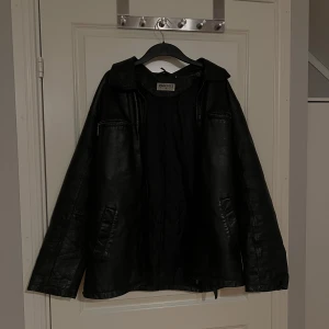 Svart skinnjacka från John F. Gee - Snygg svart skinnjacka från John F. Gee med klassisk krage och quiltat innerfoder. Jackan har dragkedjor på bröstfickorna och raka fickor på sidorna. Perfekt för dig som gillar en stilren och tidlös look.