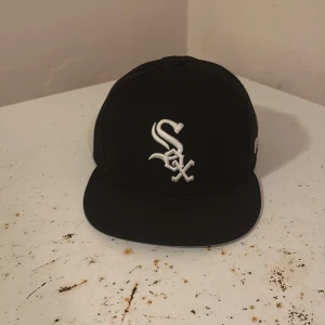 Svart White Sox keps från New Era - Snygg svart keps från New Era med Chicago White Sox-logga broderad i vitt framtill. Klassisk 59FIFTY-modell med rak skärm och MLB-logga baktill. Kepsen är tillverkad i 100% polyester och har New Era-logga på sidan.