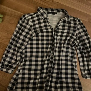 Rutig skjorta från KappAhl svart/vit - Snygg svartvit rutig skjorta från KappAhl i storlek M. Skjortan har klassisk krage, knäppning framtill och långa ärmar. Perfekt för dig som gillar en avslappnad men ändå stilren look.