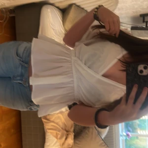 Vit omlottblus från Vero Moda XS - Supersöt vit omlottblus från Vero Moda i storlek XS. Blusen har korta, vida ärmar och markerad midja med resår. Den är i ett lätt och luftigt material, perfekt för varmare dagar. Stilren och enkel att matcha med jeans eller kjol.