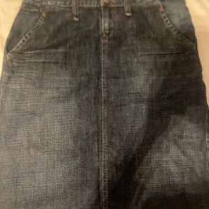 Jeanskjol från edc by Esprit, stl 40 - Mörkblå jeanskjol från edc by Esprit i klassisk modell med fickor fram och bak samt bälteshällor. Kjolen har raka linjer och är tillverkad i slitstarkt denimtyg. Perfekt för dig som gillar en tidlös och avslappnad stil.