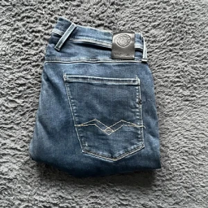 Replay jeans blå, waist 36/34 - Snygga blå jeans från Replay med klassisk femficksdesign och coola slitningar framtill. Jeansen har raka ben och tydliga kontrastsömmar på bakfickorna. Perfekta för dig som gillar en avslappnad men trendig look.