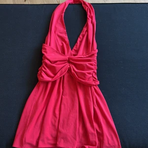 Röd halterneckklänning från Zara - Supersnygg röd kortklänning från Zara med halterneck och djup v-ringning. Klänningen har en cool draperad detalj över bysten och är öppen i ryggen.