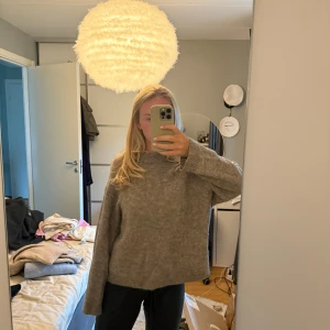 Grå/brun stickad tröja med loose fit - Mysig grå/brun stickad tröja med hög hals och långa ärmar. Modellen är loose fit och har ribbade muddar vid ärmslut och nederkant. Perfekt för dig som gillar en chill och avslappnad stil. Passar till både jeans och mjukisbyxor.