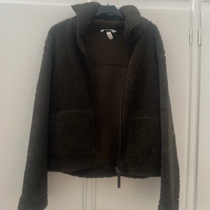Mörkbrun teddyjacka XS - Mysig mörkgrön teddyjacka i storlek XS med två stora fickor framtill och hel dragkedja. Jackan har hög krage och är tillverkad i fluffigt fleece-material som håller dig varm under kyliga dagar. Perfekt för dig som gillar en chill och avslappnad stil.