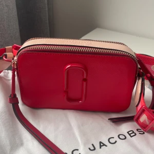 Röd axelväska - Marc Jacobs - Snygg röd axelväska från Marc Jacobs. Väskan har två dragkedjor upptill, logga framtill och en praktisk ficka på baksidan. Tillverkad i skinn och tillkommer med en dustbag.