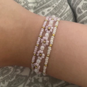Självgjort Pärlarmband Med Blommor och normala armband  - Superfint armband med små pärlor i ljusrosa, vitt och guld. Armbandet har tre rader och är dekorerat med blommor av pärlor som ger en gullig och trendig vibe. Perfekt för dig som gillar detaljer och vill ha något unikt på handleden. OBS - Pris kan diskuteras 🌷