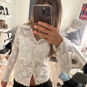 Vit spetsblus med blommönster från BySwain - Supersnygg vit spetsblus från missay med blommigt mönster och krage. Blusen är genomskinlig, har långa ärmar och knappar framtill. Perfekt för dig som gillar romantisk och feminin stil. Spetsen har fina detaljer och blusen sitter normal i passformen.