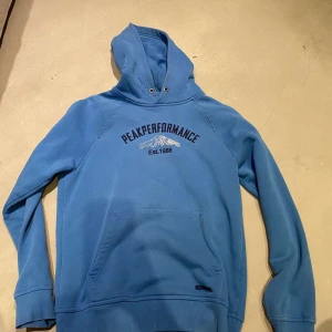 Blå hoodie från Peak Performance - Säljer en blå hoodie från Peak Performance i storlek L. Tröjan har en stor huva, magficka och tryck med logga och bergmotiv på bröstet. Tillverkad i mjuk bomull, perfekt för chill dagar. Långa ärmar och ribbade muddar för extra komfort. Pris kan sänkas till 150 vid snabbaffär! Hör av er👋