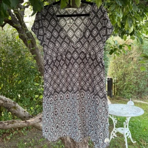 Svart kortklänning med blommigt mönster - Kortklänning med svart botten och blommigt mönster i vitt, blått och beige. V-ringad med korta ärmar och lätt utställd kjol. Tunt, mjukt tyg som känns skönt mot huden. Perfekt för varma dagar och har en bohemisk vibe. Storlek 2 som enligt deras storleksguide motsvarar en storlek M. Mycket fint skick, jag hittar inga synliga anmärkningar eller defekter.