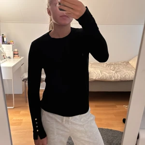 Svart långärmad tröja med knappar - Snygg svart långärmad tröja med rund hals och dekorativa silvriga knappar vid ärmsluten. 