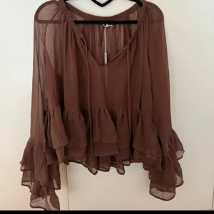 Brun volangblus med v-ringning från Gina tricot  - Säljer en brun blus med v-ringning och långa ärmar. Blusen har flera lager volanger både på ärmarna och nedtill, vilket ger en flowy och bohemisk känsla. Tunn och luftig i materialet, perfekt för dig som gillar en avslappnad men ändå trendig stil. Blusen är i storlek 36 alltså S🙈🤎🧸 Lappen sitter tyvärr ej kvar och är använd fåtal gånger men fortfarande i fint skick och perfekt höstfärg!!