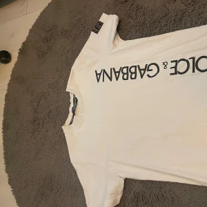 Vit t-shirt - Vit t-shirt med svart logotyptryck över bröstet och en svart etikett på ärmen. Klassisk rund halsringning och korta ärmar. Tillverkad i mjuk bomull för en skön känsla. Perfekt för dig som gillar stilrena designer med premiumkänsla.