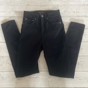 Svarta jeans från Nudie Jeans, W26 L28 - Svarta jeans från Nudie Jeans med klassisk fyrficksdesign och snygga detaljer på bakfickorna. Jeansen har smal passform och är tillverkade i mjukt bomullstyg. Perfekta för dig som gillar stilrena och tidlösa byxor. Jeansen är i väldigtbra skick. W26 L28 säljs för 400kr, kontakta om frågor 