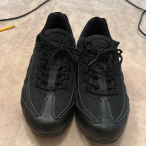 Svarta Nike Air Max sneakers - Säljer ett par helsvarta Nike Air Max sneakers med klassisk chunky sula och mesh- samt skinnpaneler. Skorna har snörning och diskreta Nike-loggor på både häl och plös. Perfekta för dig som gillar en clean och sportig look.