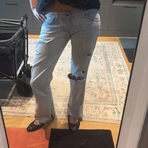 Ljusblå slitna bootcut jeans Wrangler - Ljusblå jeans från Wrangler med bootcut passform och råa, fransiga benslut. Jeansen har flera slitningar och hål på benen för en edgy look. Klassisk femficksmodell med låg midja och Wrangler-logga på bakfickan. Perfekta för dig som gillar vintagevibbar. Använda en del, där av lite slitna ner. 