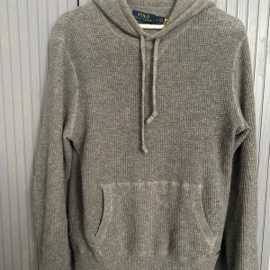 Grå kashmirhoodie från Polo Ralph Lauren - Supermjuk grå hoodie i 100% tvättbar kashmir från Polo Ralph Lauren. Ribbstickad struktur, huva med snörning och magificka framtill. Inga defekter förutom lappen inuti tröjan. Köpt för 5500kr