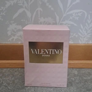 Valentino Donna Eau de Parfum 100ml - Lyxig parfym från Valentino, Donna Eau de Parfum i 100 ml flaska. Flaskan är elegant med mönstrat glas och gulddetaljer, och kommer i en ljusrosa ask med guldplatta. Doften är feminin och exklusiv, perfekt för dig som vill sticka ut.