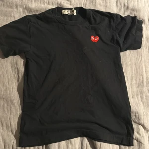 Svart Comme des Garçons Play t-shirt - Svart t-shirt från Comme des Garçons Play med klassiskt rött hjärta med ögon broderat på bröstet. T-shirten har rund halsringning och korta ärmar. Tillverkad i mjuk bomull och har en clean, stilren look som passar perfekt till jeans eller shorts. Pris är inte hugget i sten.